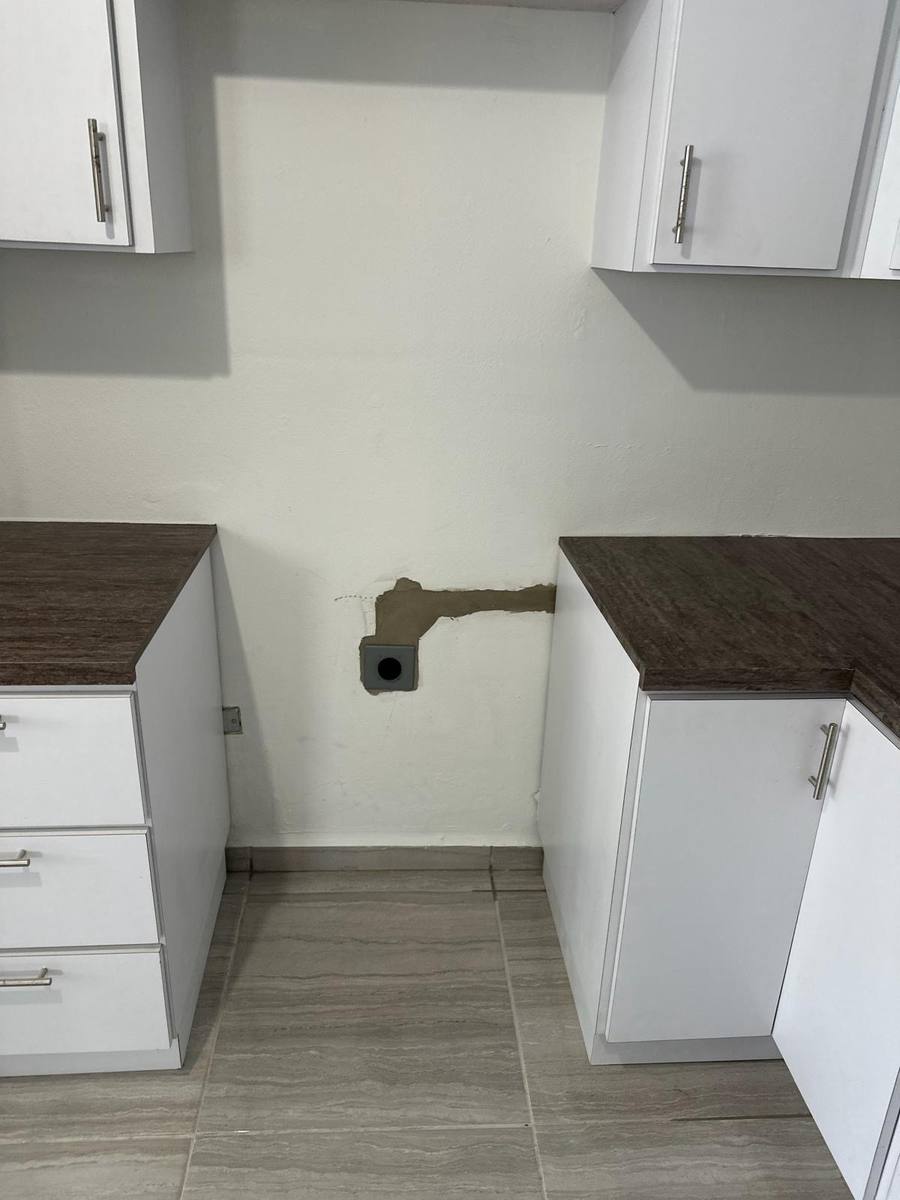 A new outlet box stubbed out of a kitchen wall between two cabinet banks, with the wall chase above it patched and skim-coated.